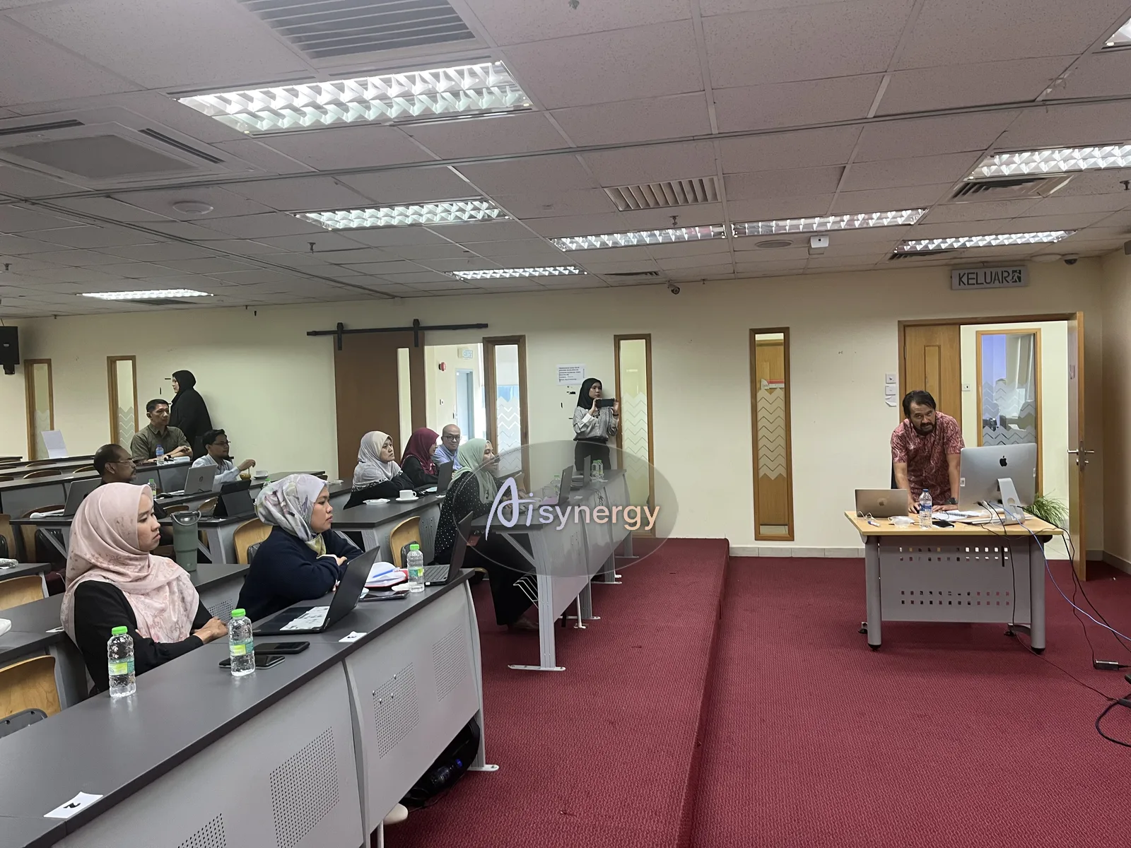 Wide view of a training room with the trainer at the front and participants at desks