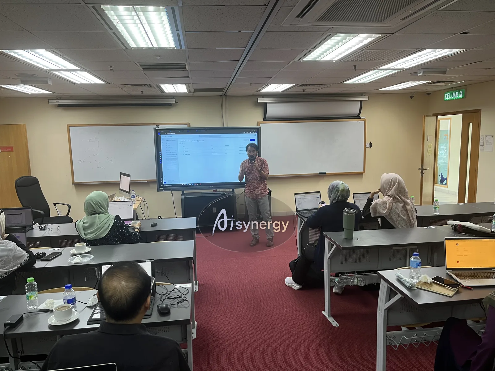 AISynergy trainer presenting at the screen while participants follow on their laptops